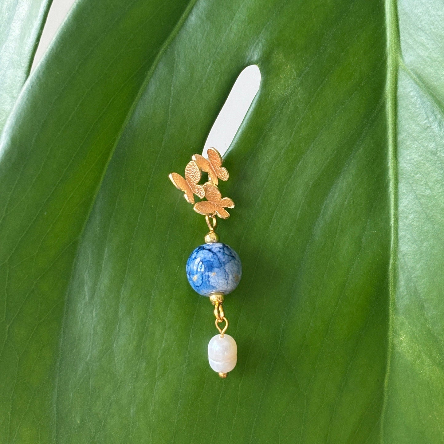 Decorative hair clip with blue bead and gold accents on a green leaf background