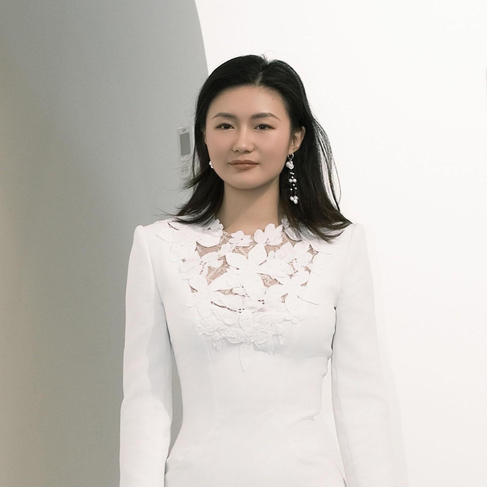 Woman wearing handcrafted mini ceramic teapot gracefully cascading freshwater pearls and a white dress with floral lace details against a plain background