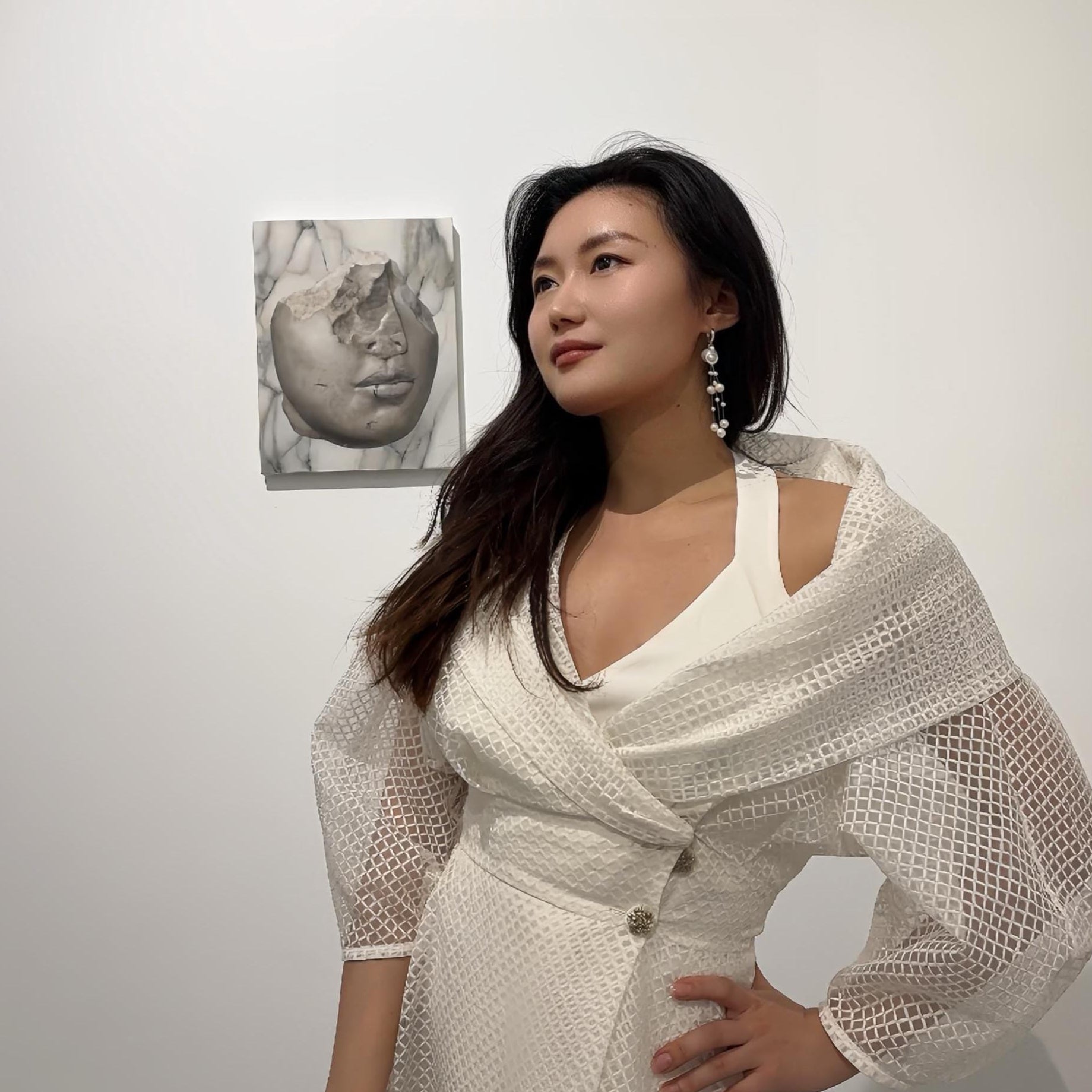 Woman wearing a handcrafted mini ceramic teapot gracefully cascading freshwater pearls and a white dress with  a beige shawl in a minimalistic setting.