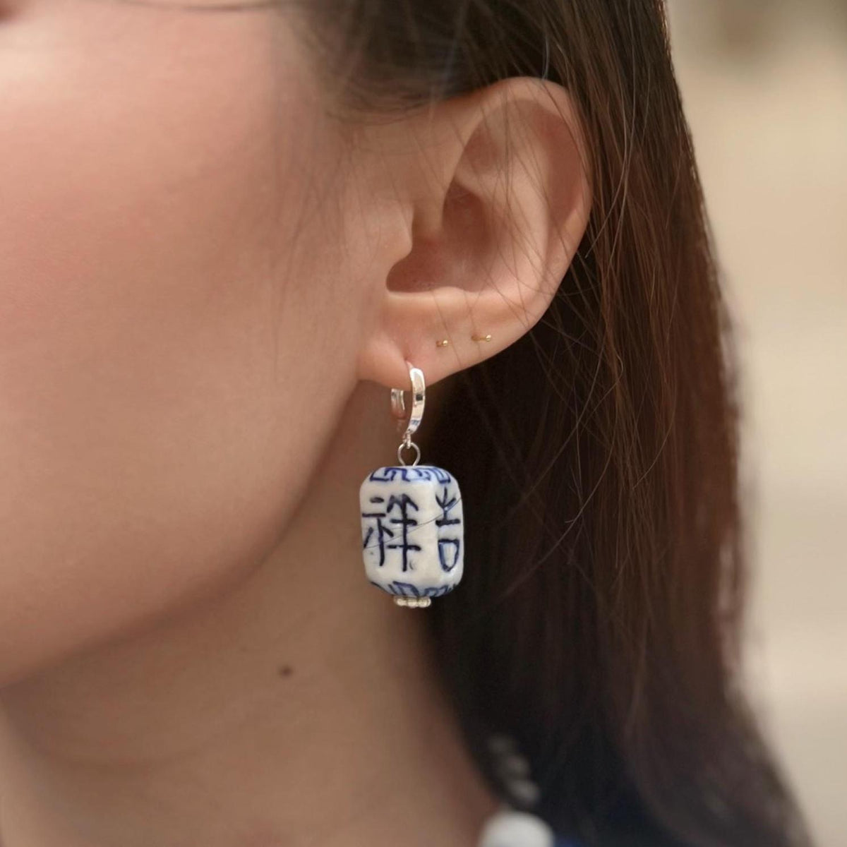 Close-up of an ear wearing a blue and white earring with Chinese characters.