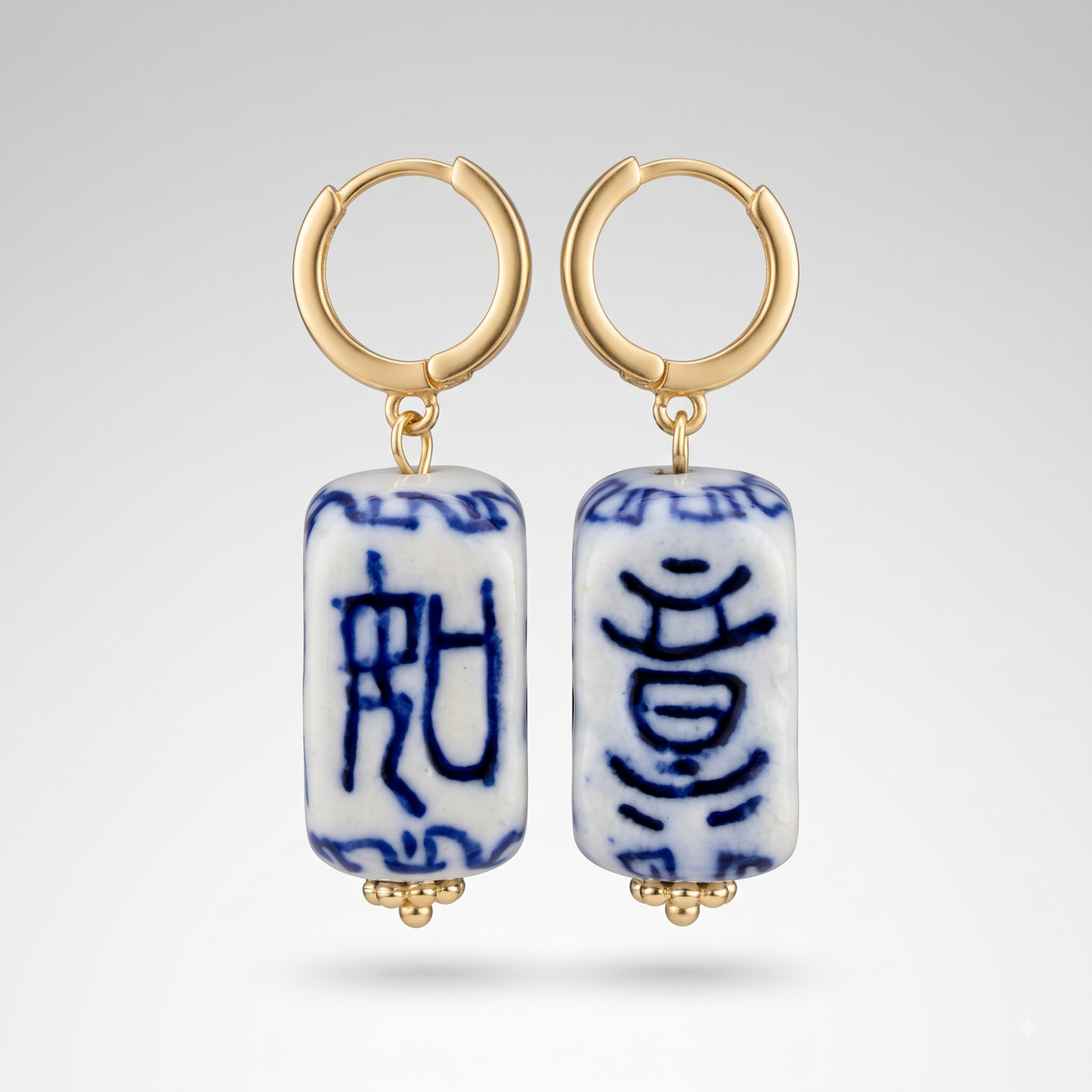 A pair of gold hoop earrings with rectangular white ceramic pendant beads featuring blue Chinese calligraphy characters, displayed against a light gray gradient background.