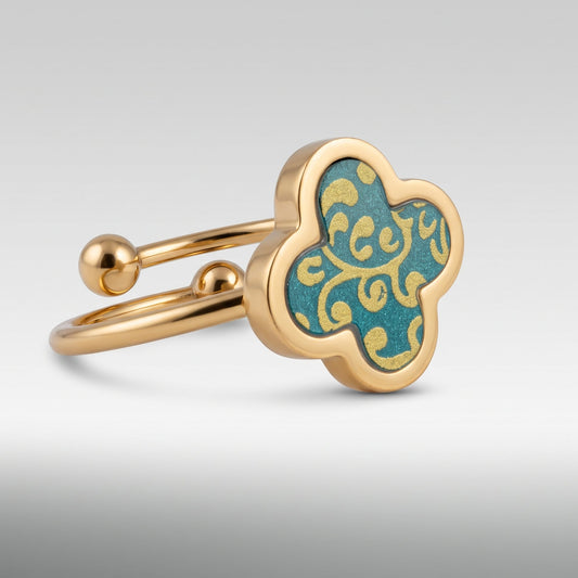 A gold-plated adjustable ring with a four-lobed clover-shaped face featuring a turquoise blue enamel background decorated with a gold filigree pattern.