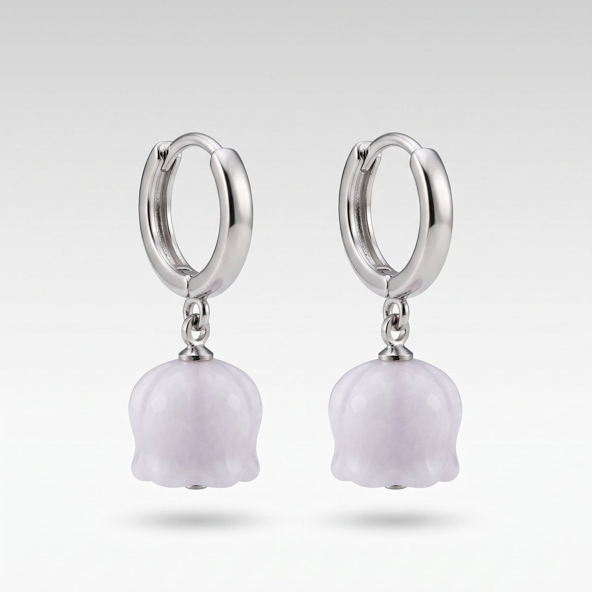 A pair of silver huggie hoop earrings with dangling light purple lily-of-the-valley flower charms, shown against a neutral light gray background.