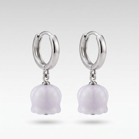 A pair of silver huggie hoop earrings with dangling light purple lily-of-the-valley flower charms, shown against a neutral light gray background.