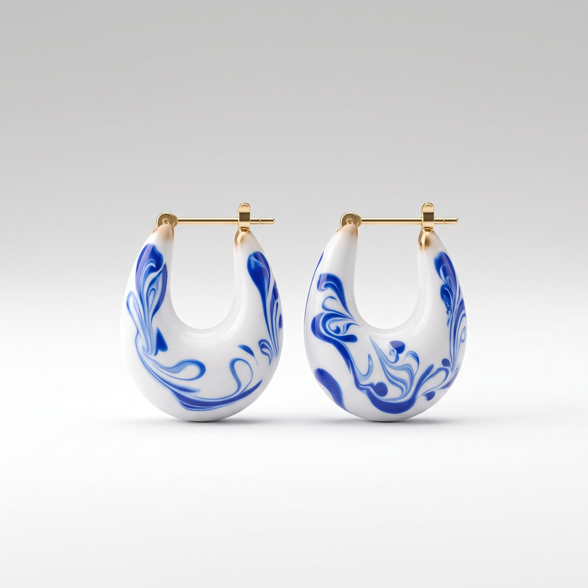 A pair of white U-shaped hoop earrings with blue marbled swirl patterns and gold-tone posts, shown against a clean light gray gradient background.