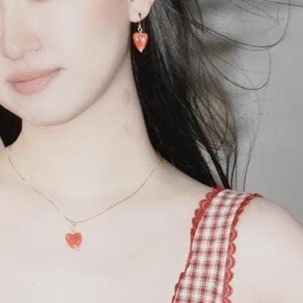 A person wearing porcelain heart hoop earrings with a red glaze, paired with gold-colored hoops, and a red and white checkered top.