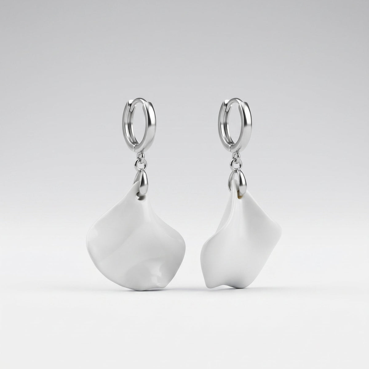 A pair of silver hoop earrings with large, organic-shaped white drop charms, displayed against a clean light gray gradient background.