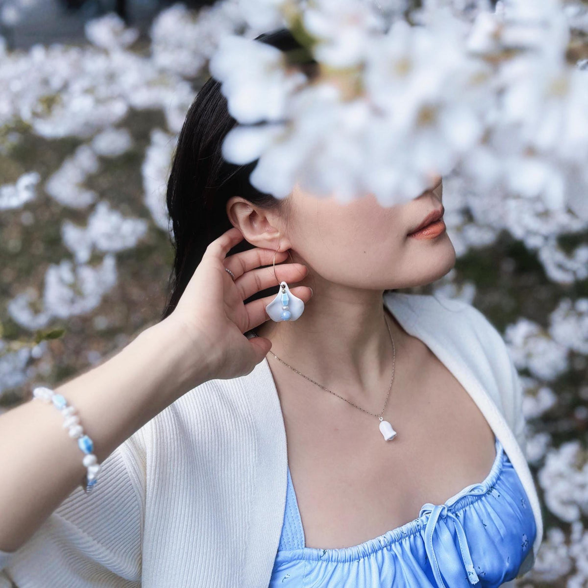 Woman wearing pearl earrings and necklace with cherry blossoms in the background