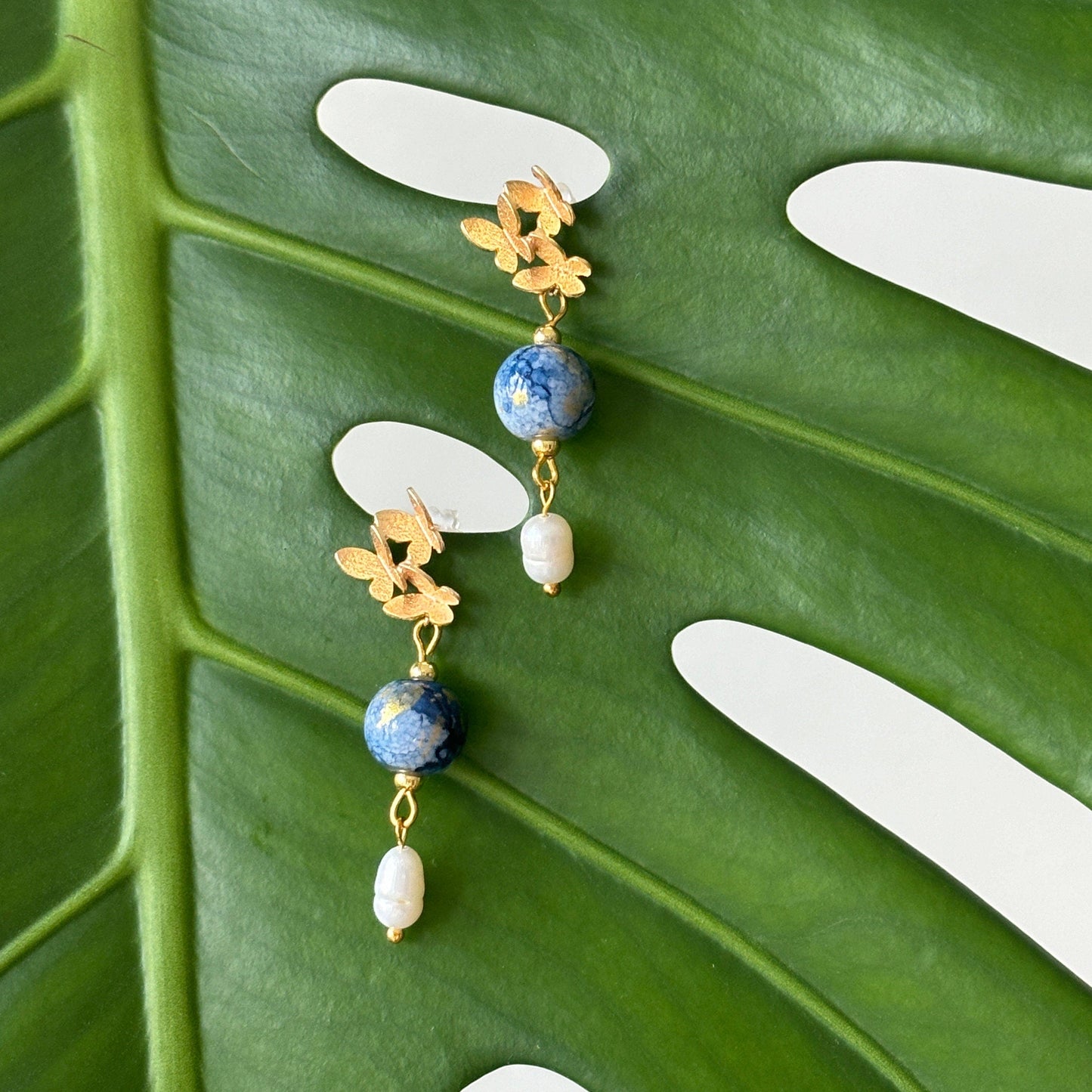 Gold earrings with blue beads and pearls on a green leaf