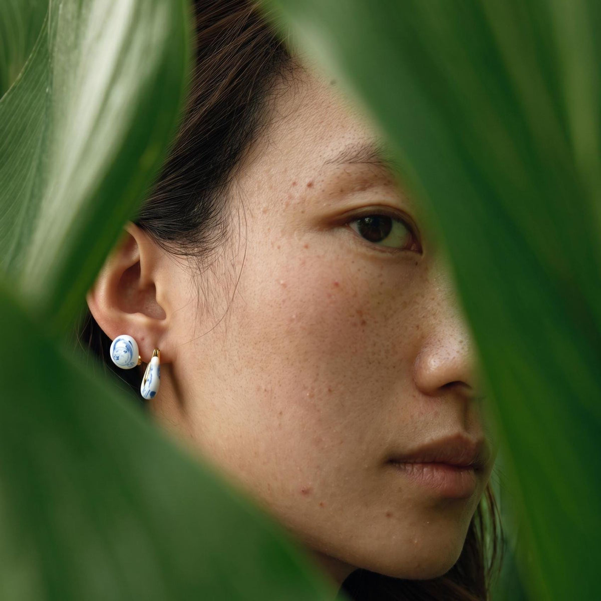 Close-up of a person wearing earrings with green leaves in the foreground