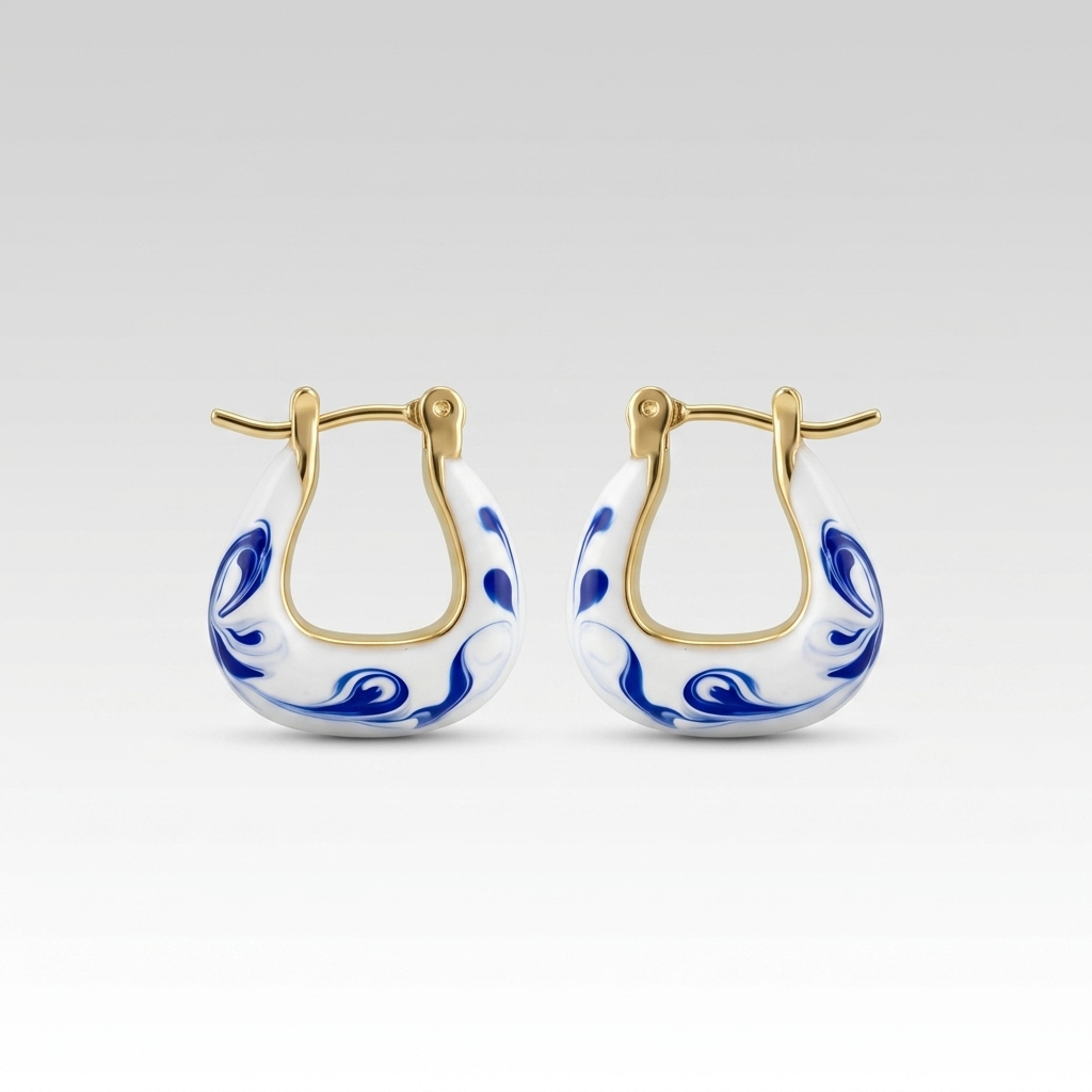 A pair of small hoop earrings with gold-tone metal hoops and white enamel inserts decorated with blue swirled patterns, shown on a light gray gradient background.
