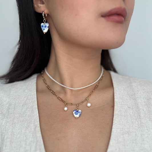 Close-up of a person wearing a necklace with heart-shaped blue gemstones and pearl accents.