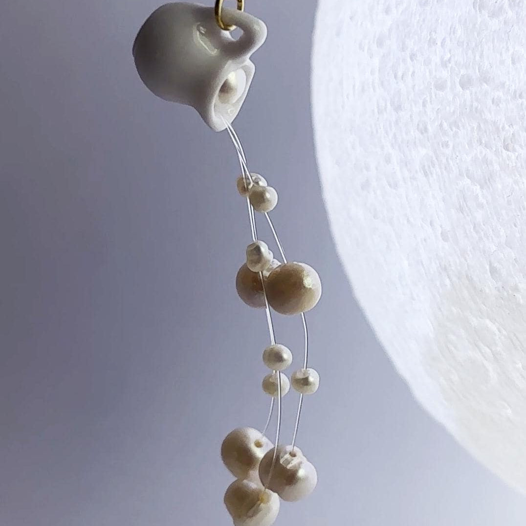 Earring with ceramic teacup and pearl-like beads on a light gray background