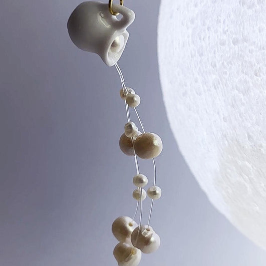 Earring with ceramic teacup and pearl-like beads on a light gray background