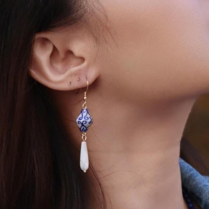 Close-up of an ear wearing a blue and white earring with a gold hook.