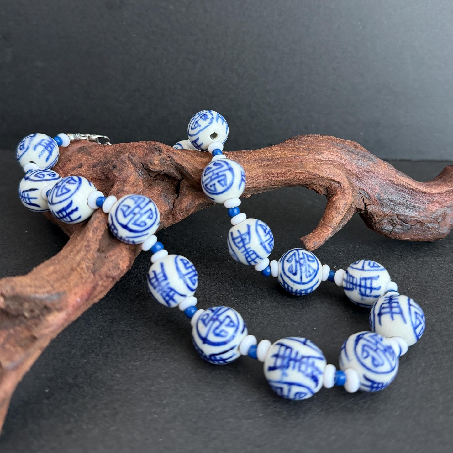 Blue and white ceramic beads with Chinese characters, displayed on a piece of natural driftwood against a dark gray background.