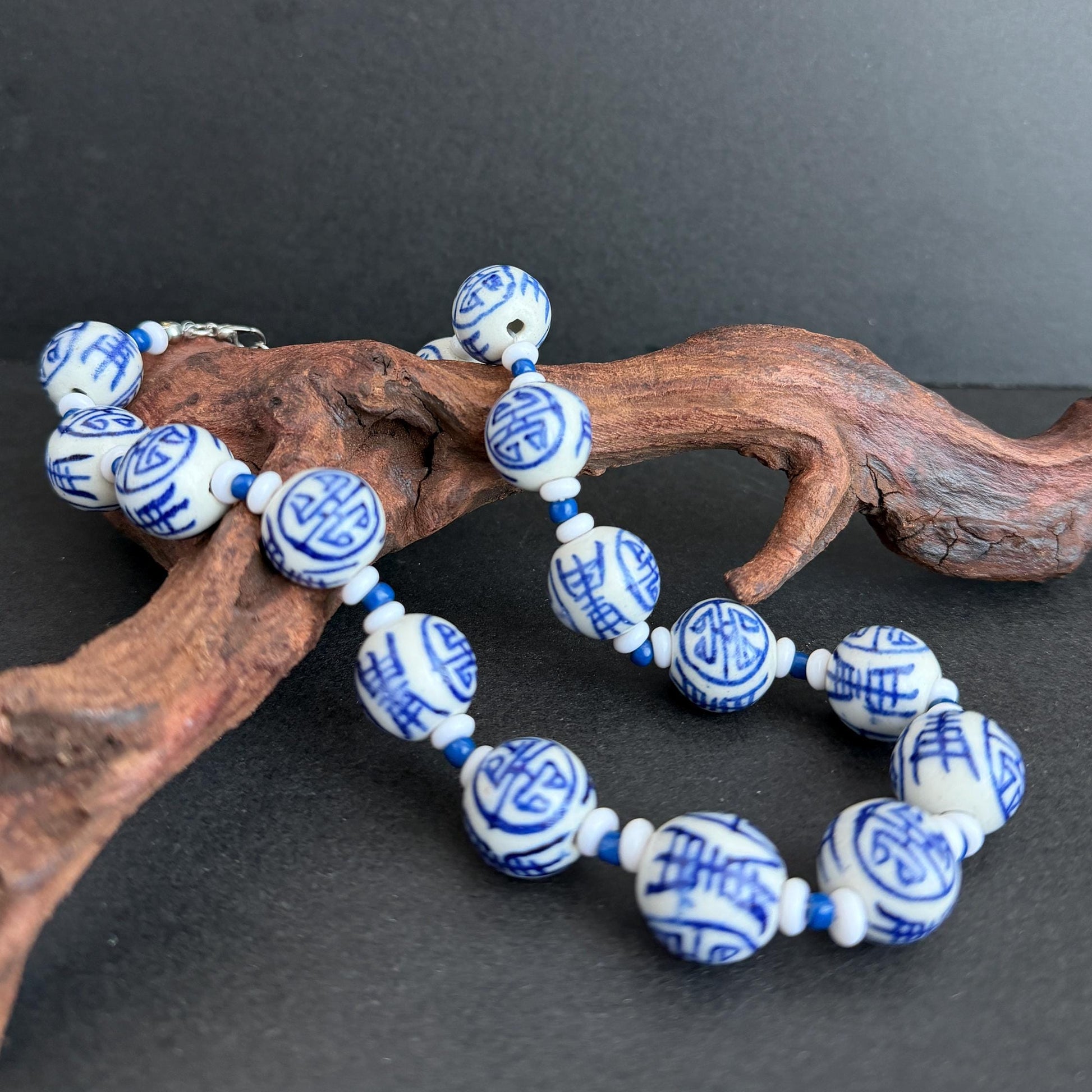 Blue and white ceramic beads with Chinese characters, displayed on a piece of natural driftwood against a dark gray background.