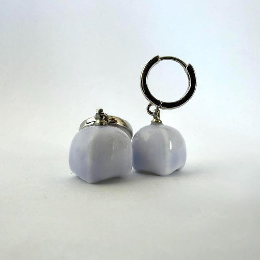 A pair of earrings featuring smooth, rounded pale lavender-blue stone pendants hanging from silver-toned hoop backings, shown on a plain light background.