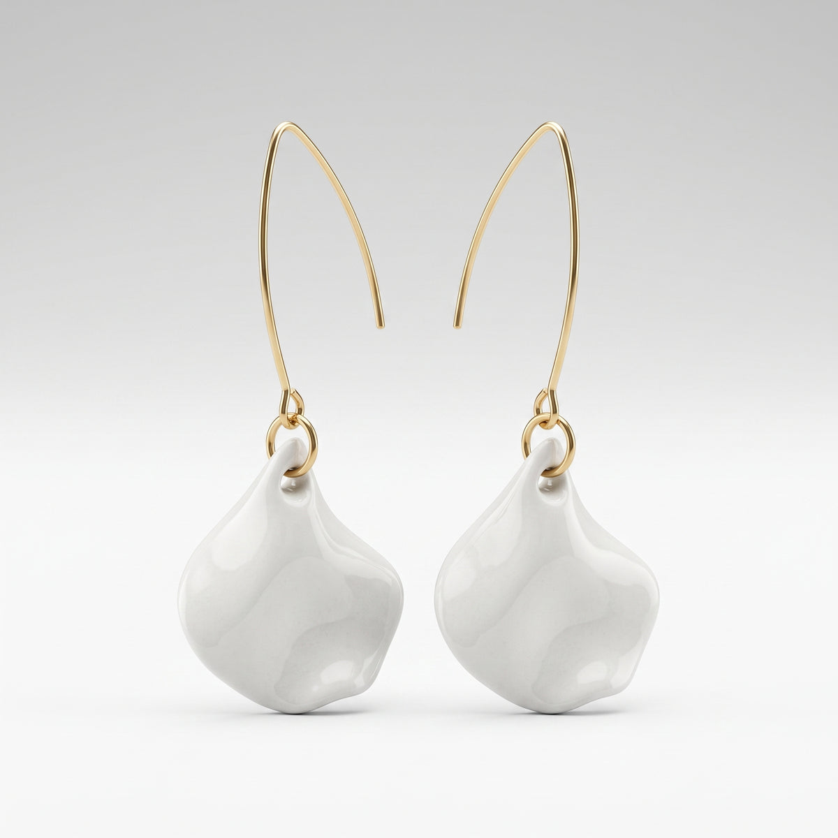 A pair of modern dangle earrings featuring organic, wavy white ceramic drops suspended from sleek, curved gold ear wires, set against a clean light gray gradient background.